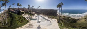 Drone panoramic of a mansion with a pool and palm trees on top of a bluff overlooking the ocean and Blacks Beach