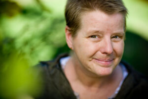 close-up portrait of a short haired woman smiling and framed with soft green hues