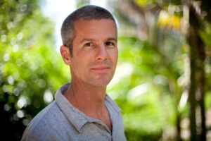 Experimental high speed shutter and snooted flash portrait of Chris Keeney with green plants and palm trees behind him