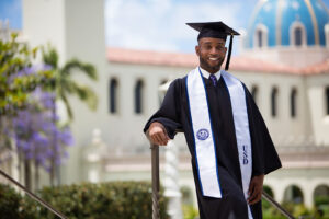 University of San Diego graduate portrait photography of black student leaning against railing with The Immaculata Church in the background