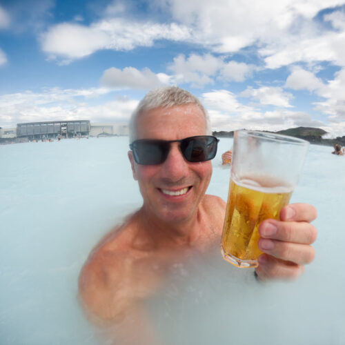 Photo of Chris Keeney wearing sunglasses and drinking a beer at the Blue Lagoon which is located in Southwestern Iceland. The water is a light turquoise color due to the silt in the water.