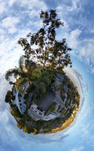 360 degree world view panoramic photograph of a neighborhood in Summerland Santa Barbara with large tree in foreground and sunsetting in the background surrounded by blue sky and white puffy clouds.