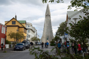 Looking through some trees on Skólavörðustígur street at the Hallgrímskirkja Church with people walking around colorful red, white and yellow buildings.