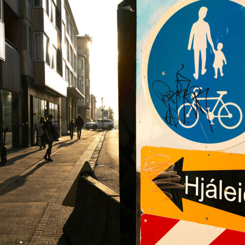 Bright afternoon sunlight shining on the street of Reykjavík Iceland with people walking on the side walk and colorful street signs in the foreground
