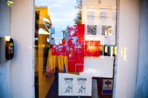Multi-dimensional image with a Red Cross in the center of the photo. People walking on the street reflected the glass door of the building in Reykjavík Iceland