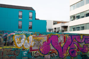 A wall covered with graffiti art in front of some turquoise and white Scandinavian style architecture buildings on the streets of Reykjavík, Iceland