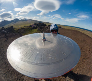 A woman standing behind a large round shiny metal sundial at the Saxhóll Crater in Snæfellsjökull National Park