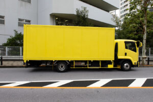 Light yellow truck parked on the street in Tokyo Japan on an overcast fall day. The bright yellow of the truck and the black and white stripes in the street make for a dynamic high contrast photographic composition.