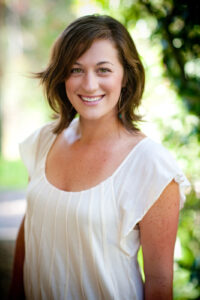 color headshot portrait photograph of a brunette woman in her mid thirties standing in a garden while smiling at the camera