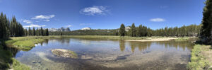 panoramic photo of the Tuolumne River in The Tuolumne Meadows with blue skies and small white fluffy clouds
