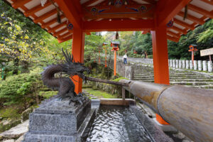 color photograph of a brass dragon head with water coming out of his mouth into a bamboo ramp that feeds into a stone wash basin for people to cleanse their hands before entering the Shinto temple of Kumano Nachi Taisha