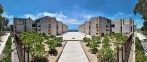 One hundred and eighty degree drone panoramic photograph looking West at the Salk Institute's courtyard and South and North towers. You can also see parts of the grove and orange trees in the foreground