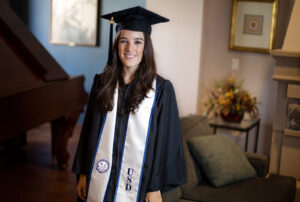color photograph of a University of San Diego female graduate in cap, gown and stole inside a meeting room with a piano