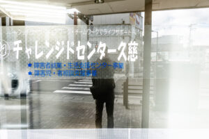 a photo of a reflection of a person looking through a window on a street with white and blue Japanese kanji