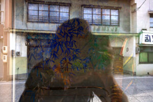 abstract color photograph of a reflection of Chris Keeney in the store window in Setoda, Japan.