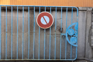 a light blue painted metal gate with a red circular no entry sign in front of concrete wall and orange pained building behind.
