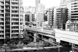 Black and white high contrast photograph of the buildings, metro and streets of Tokyo seen from the train