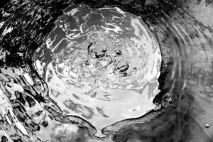 Black and white abstract photograph of water bubbling up from a hot spring in Beppu, Japan. A main organic circular shape with other grayscale forms interacting with it.