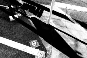 black and white abstract high contrast photograph of graphic markings on a parking lot in Nachikatsuura, Japan. Diagonal black and white shapes with round metal anchor points in the textured asphalt.