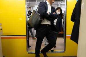 color photograph of business people dressed in black and white getting off a yellow train on the Tokyo metro