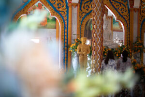 Artistic Interior view of the Wat Chalong Buddhist Temple in Phuket Thailand. Gold, blue white and green decorations, flowers and a seated Buddha