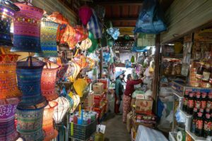 Colorful lanterns inside a narrow stall at Hoi An Central Market (Cho Hoi An), Vietnam, with vendors organizing goods in a busy aisle.